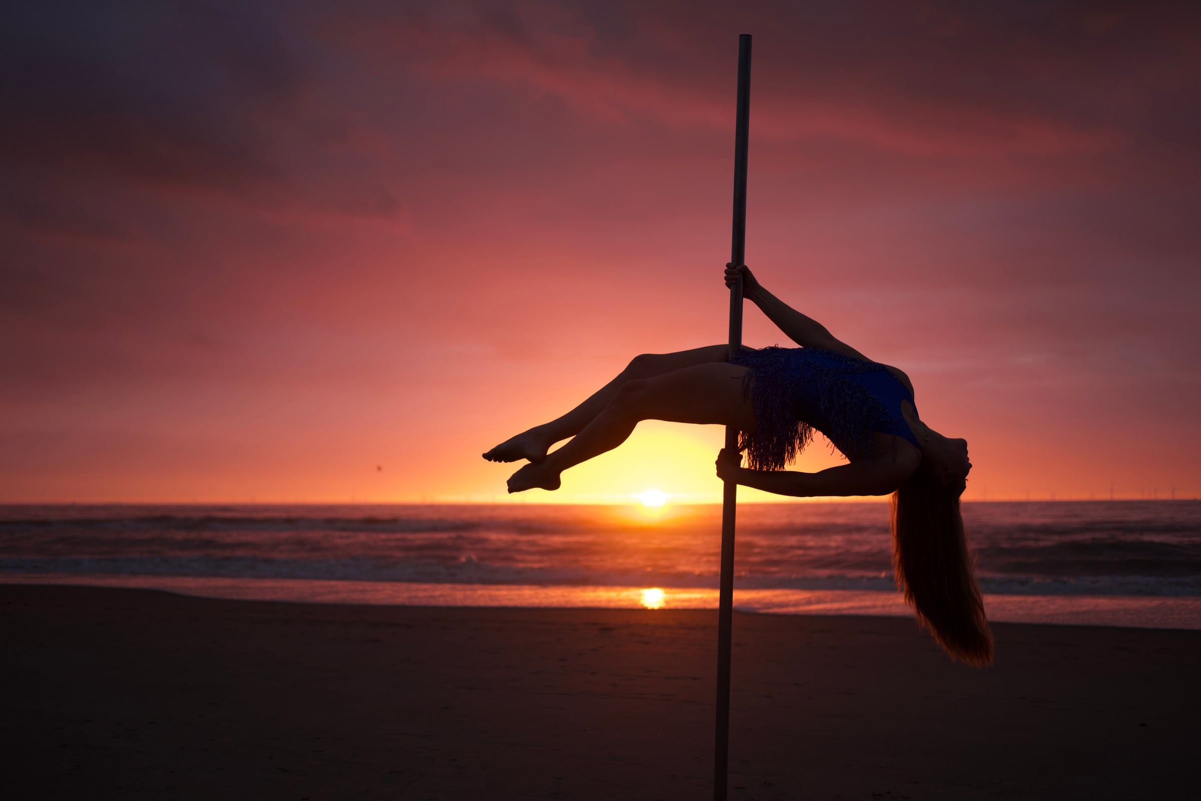Megan Konings in a backbend on the pole, silhouetted against the setting sun over the sea