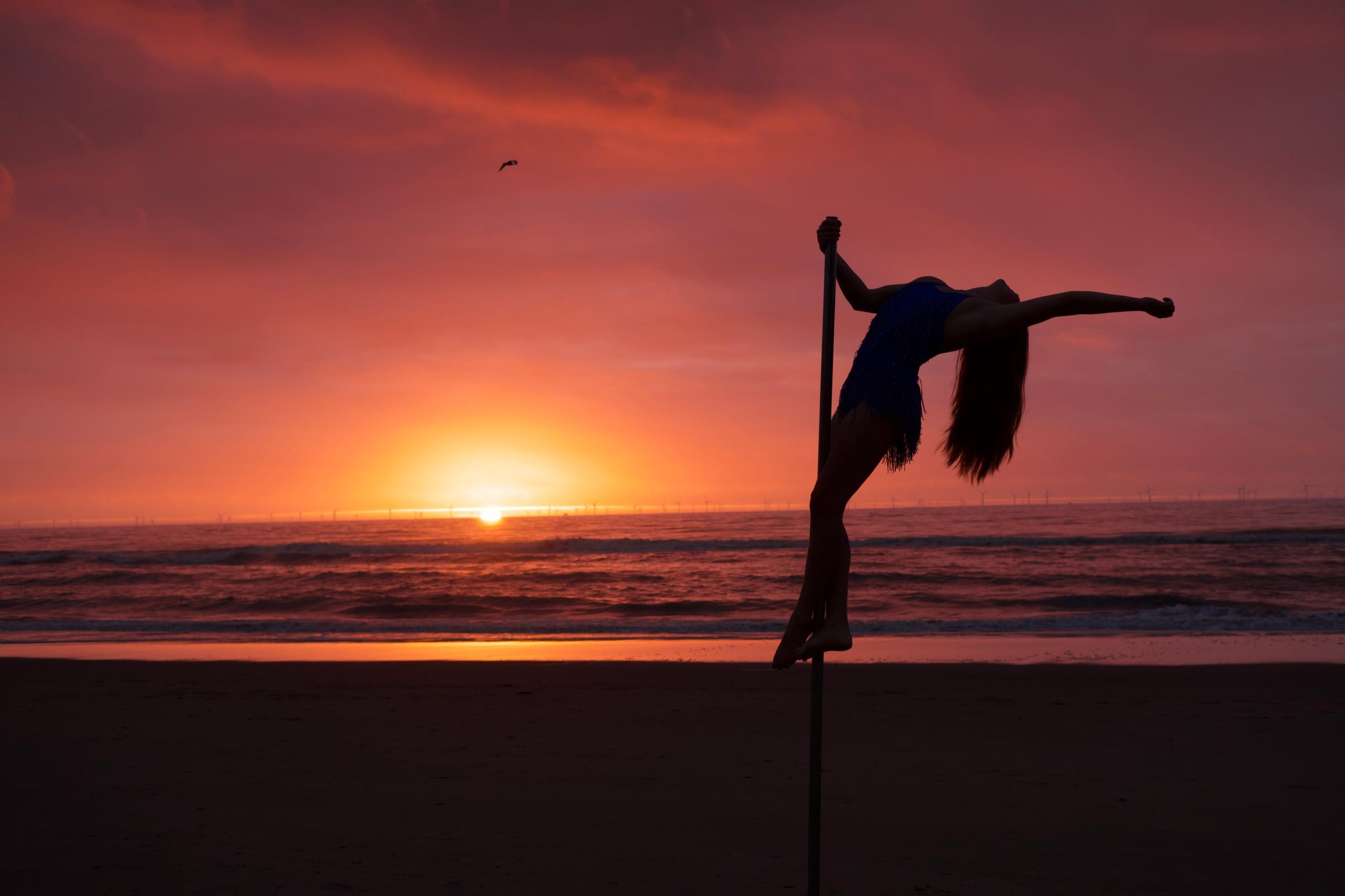 Megan reaching out from the pole with one arm extended against a red sky