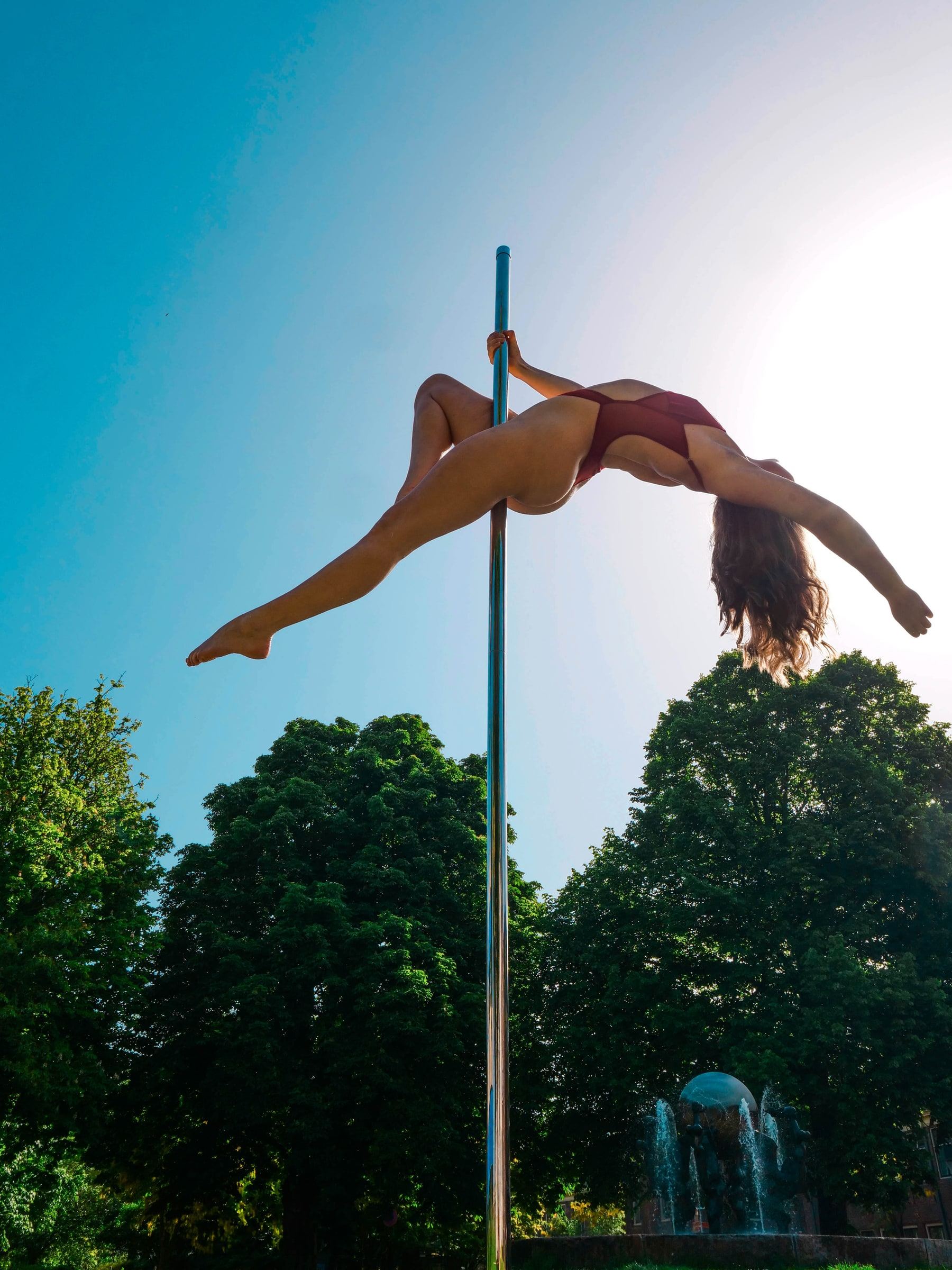 Megan Konings in an open backbend on the pole against a bright summer sky
