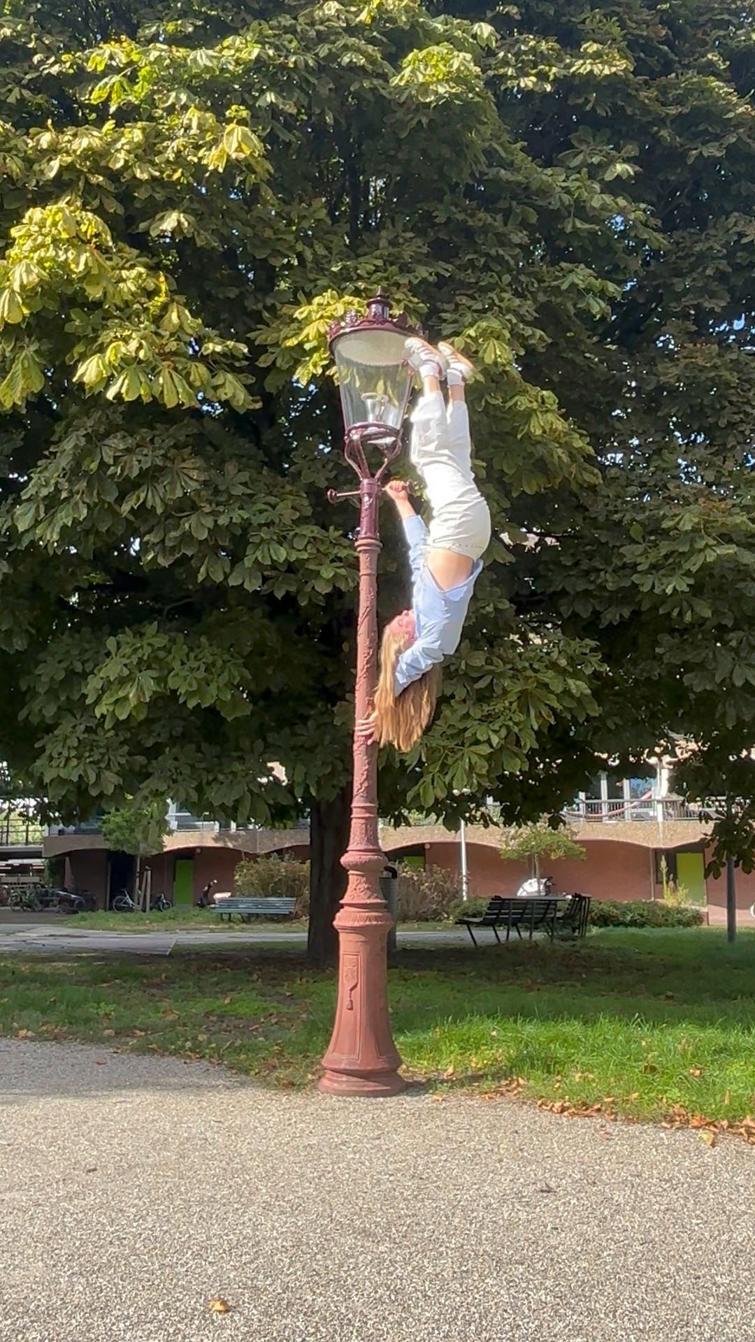 Megan Konings inverted on a street lamppost in a park